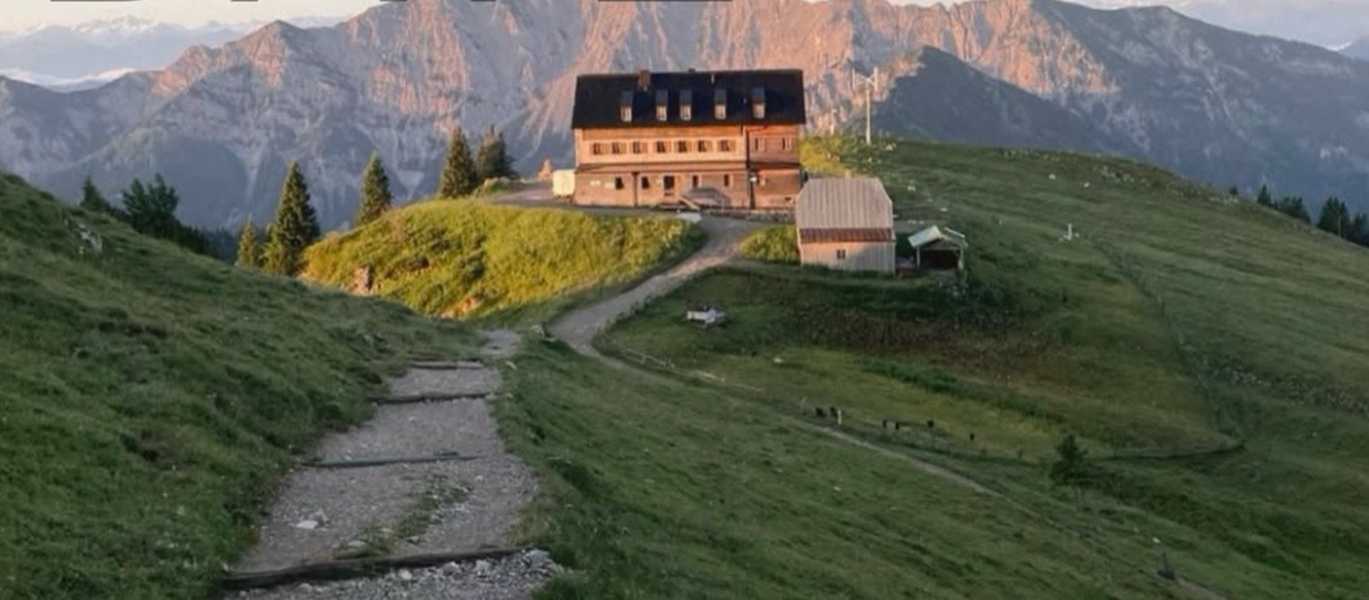 Berghütte auf einem Almrücken vor Bergpanorama bei Abendlicht